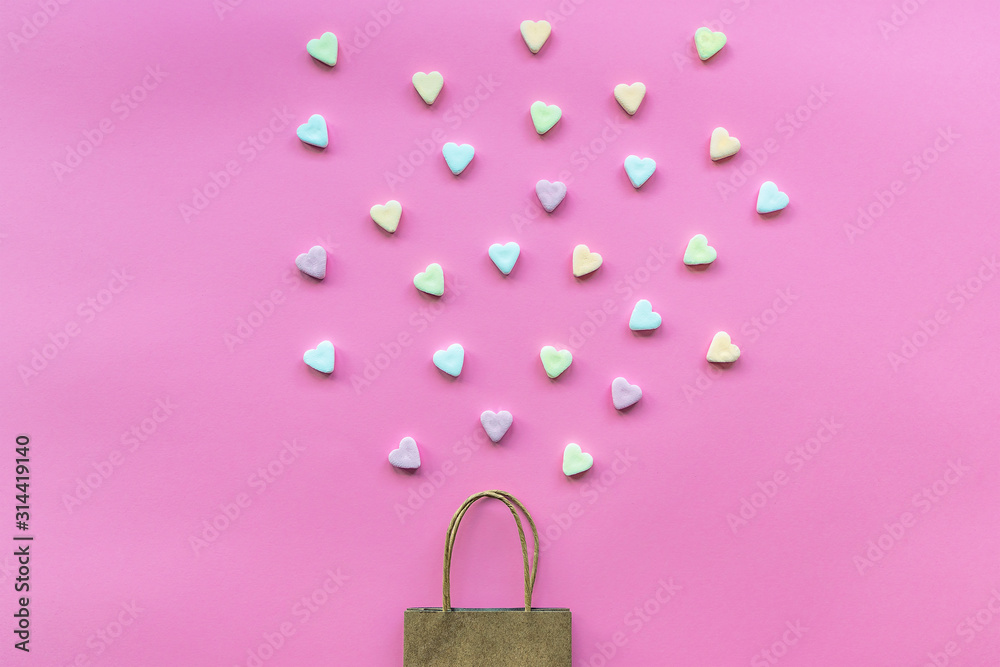 Obraz premium Gift bag with scattered hearts sweets on a pink background. Valentine's Day present concept. Top view, flat lay.