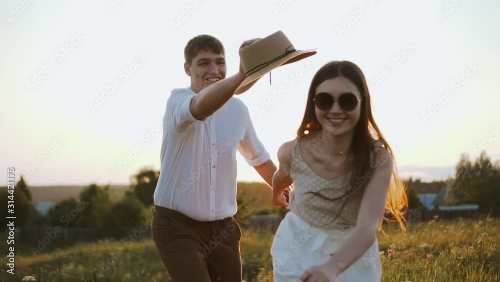 Millennials stylish couple have fun playing with hat, running and catching each other. They enjoy sunset outdoors, walking together in beautiful meadow. Careless and happy boyfriend and girlfriend Millennials stylish couple have fun playing with hat, running and catching each other. They enjoy sunset outdoors, walking together in beautiful meadow. Careless and happy boyfriend and girlfriend