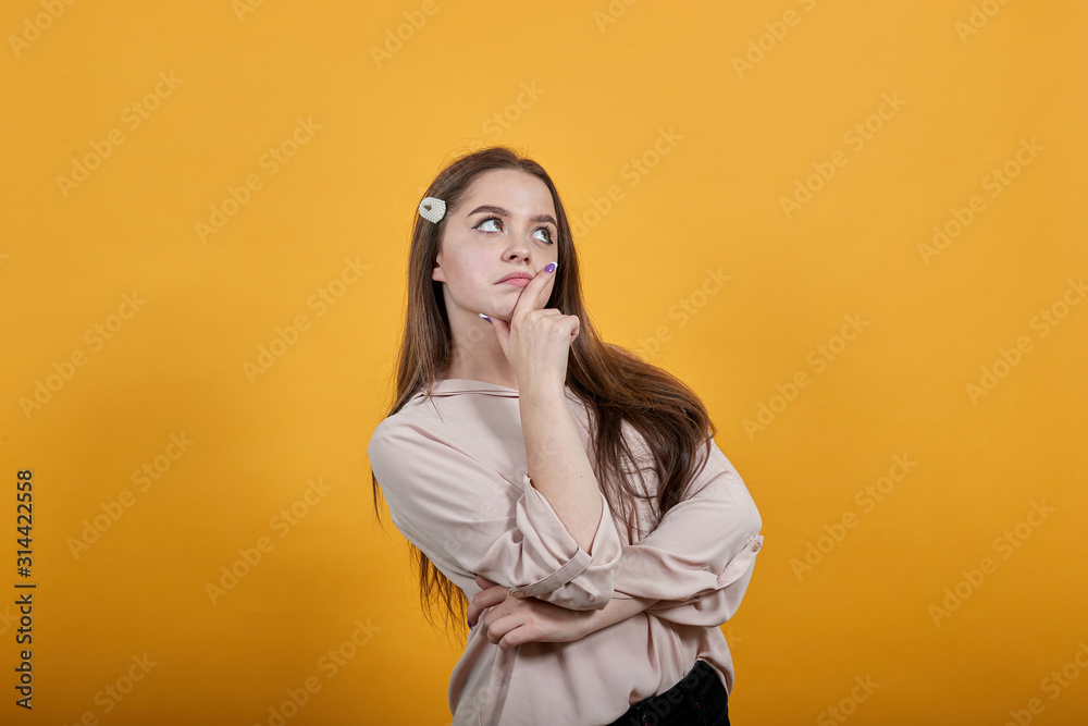 Attractive caucasian young woman staying sideways, hugging her stomach, thinking wearing fashion pastel shirt isolated on orange background in studio. People sincere emotions, lifestyle concept.