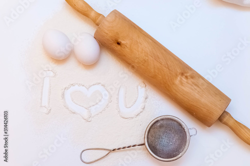 inscription i love you on flour. near a rolling pin, eggs and a sieve.