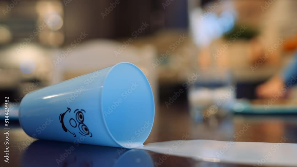 Toddler accidentally spills cup of milk on the table and mother wipes it up