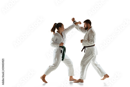 Junior in kimono practicing hand-to-hand combat with coach, martial arts. Young female mongol fighter with green belt training on white studio background. Concept of healthy lifestyle, sport, action.