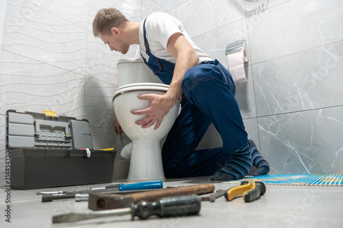 man plumber in uniform installing toilet bowl using instrument kit professional repair service photo