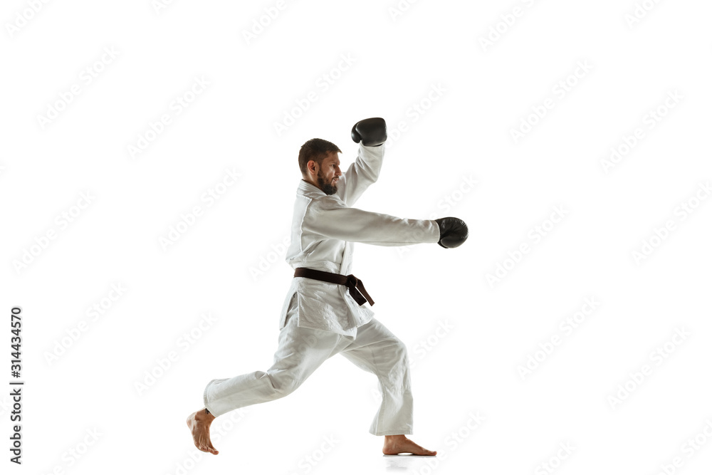 Confident coach in kimono practicing hand-to-hand combat, martial arts. Young male caucasian fighter with black belt training on white studio background. Concept of healthy lifestyle, sport, action.