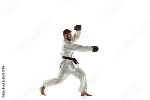 Confident coach in kimono practicing hand-to-hand combat, martial arts. Young male caucasian fighter with black belt training on white studio background. Concept of healthy lifestyle, sport, action.