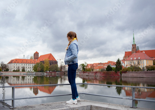  girl in a denim jacket stands with his back on the promenade and looks at the river