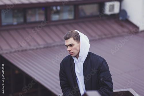 fashionable man in hood and winter clothes is posing near in street