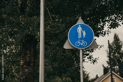 Blue road sign pedestrian and bicycle zone on green trees background.