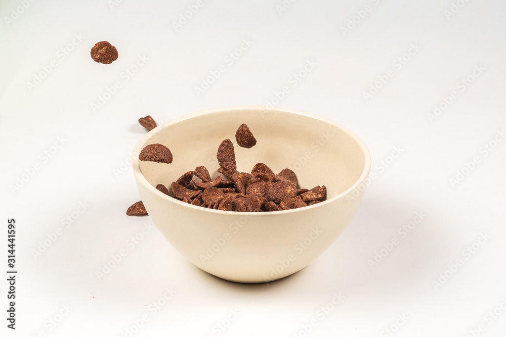 Chocolate corn flakes falling to the white bowl isolated on white. Motion. Chocolate corn flakes falling to the white bowl isolated on white. Motion.
