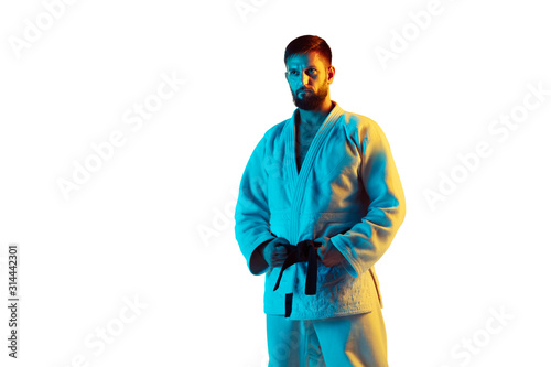 Guarding. Confident coach in kimono practicing hand-to-hand combat, martial arts. Young male fighter with black belt posing on white studio background in neon. Concept of emotions, sport, action.