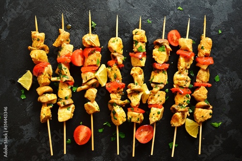 Traditional greek dish souvlaki. Kebabs on wooden skewers. Shish kebabs with tomatoes, mushrooms, pepper and lemon, top view, black concrete background. Place for text.