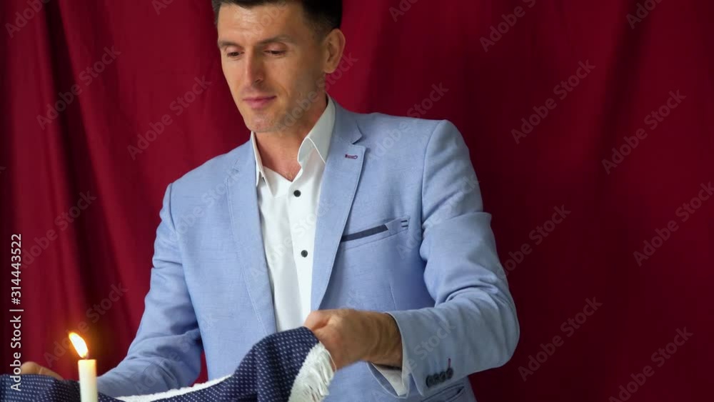 Magician in a suit shows a trick with table and candle on a vinous background