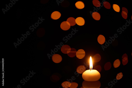 burning candle glowing in dark with bokeh lights on background