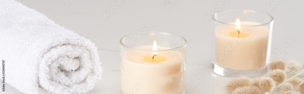 fluffy bunny tail grass near burning white candles in glass and rolled towel on marble white surface, panoramic shot fluffy bunny tail grass near burning white candles in glass and rolled towel on marble white surface, panoramic shot