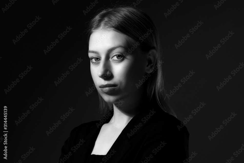 Blonde with long hair in a black suit on black background, black and white. Business woman