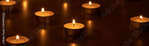 selective focus of burning white candles glowing in dark, panoramic shot