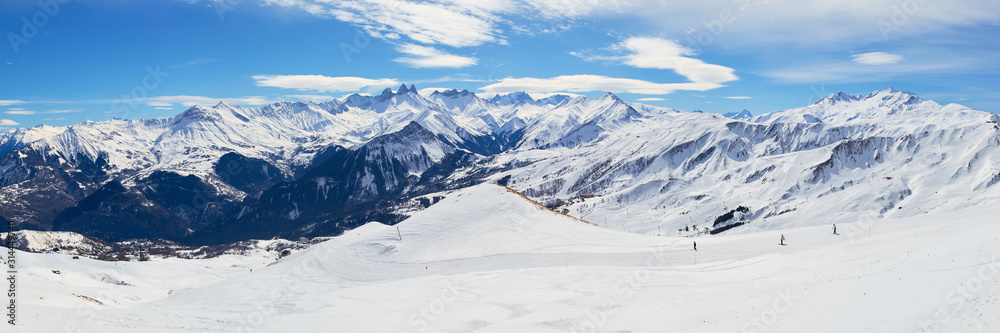 Les Sybelles ski domain in France. Panorama with slopes, skiers, and mountain peaks, on a sunny day with blue sky.