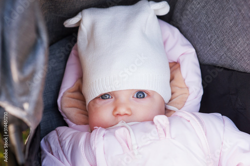 Close-up portrait of cute beautiful baby girl copeck in stroller outdoors. Infant on walk, healthy lifestyle