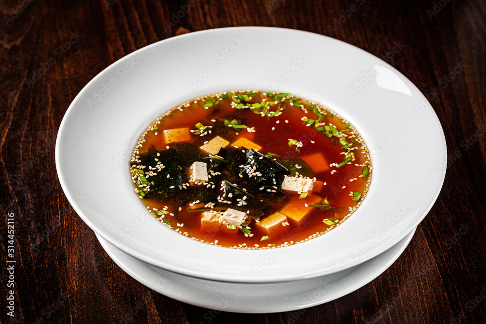 Asian cuisine. Japanese miso soup made from tofu cheese, seaweed and sesame seeds. Serving dishes in a restaurant in a white plate. background image, copy space Asian cuisine. Japanese miso soup made from tofu cheese, seaweed and sesame seeds. Serving dishes in a restaurant in a white plate. background image, copy space