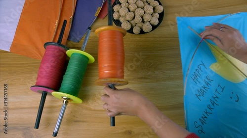 Woman hands picking up a colorful kite and charkhi to fly a kite on Makar Sankranti. Top view shot of a decorated wooden table with paper kites  designer reel charkhis  and til ladoos during Makar ... photo