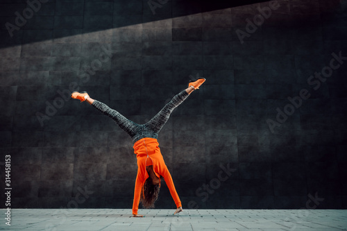 Full length of fit sporty caucasian woman in sportswear doing cartwheel exercise in front of black wall. photo