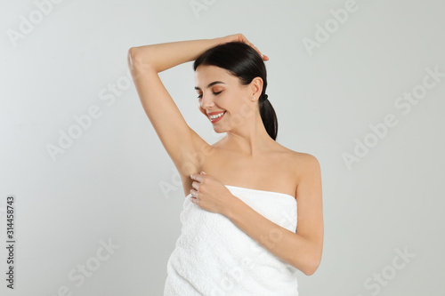 Young woman showing hairless armpit after epilation procedure on light grey background
