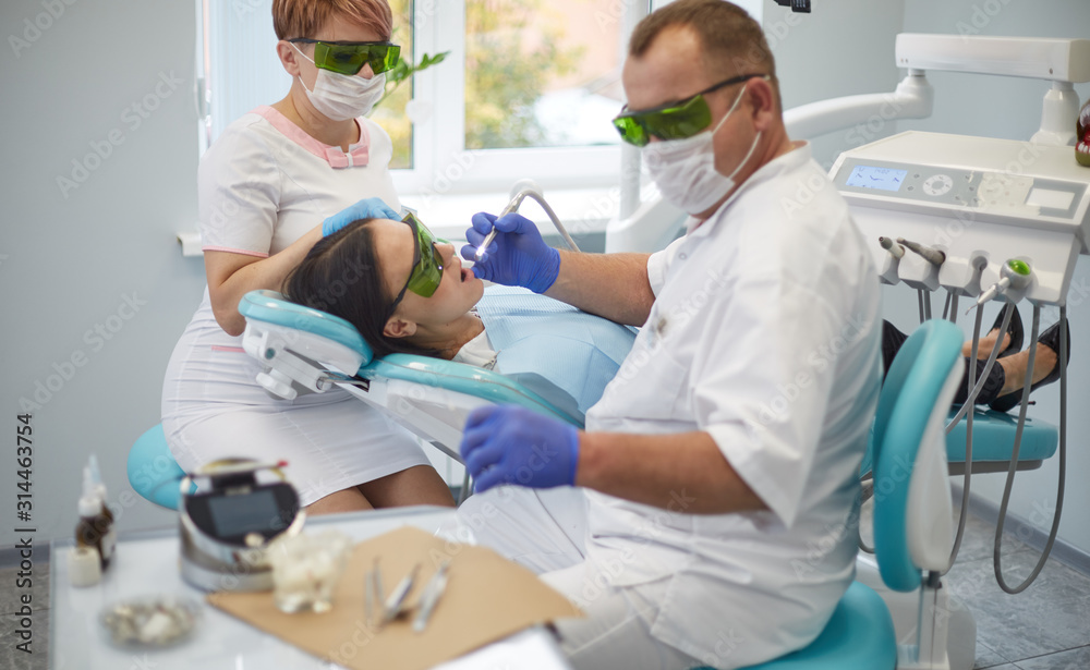 Fototapeta premium Doctor dentist treats teeth of a beautiful young girl patient. The girl on reception at the dentist. Doctor dentist treats tooth