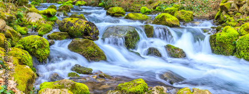 A small stream with a waterfall and mossy rocks in spring, panoramic image © liptakrobi