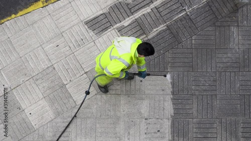 Top view of a Worker cleaning the street sidewalk with high pressure water jet. Public maintenance concept