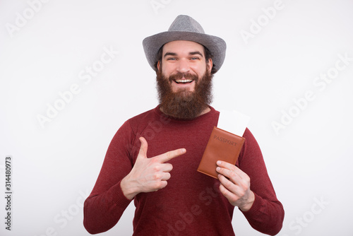 Photo of smiling man with beard pointing at passport with tickets