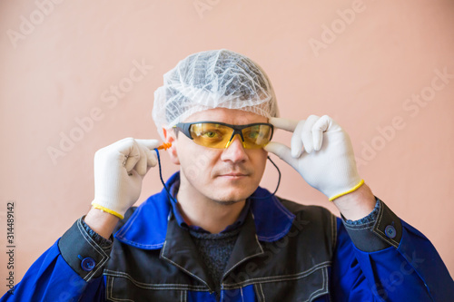 A man in special clothes in white gloves, a hat, protective glasses, earplugs in a food processing plant. Requirements for clothing in food production. photo