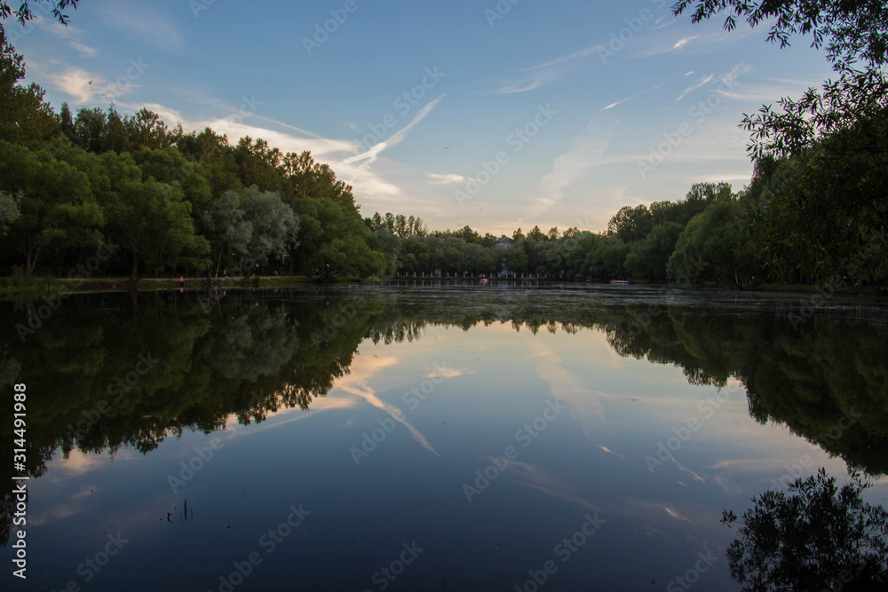 Yaroslavl. Warm evening in Neftyanik Park. Park refinery. Reflection of colorful sunset in the lake. Peace and quiet surrounded by green trees