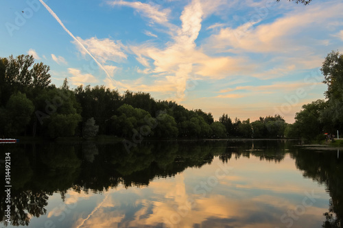 Yaroslavl. Warm evening in Neftyanik Park. Park refinery. Reflection of colorful sunset in the lake. Peace and quiet surrounded by green trees photo