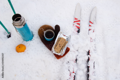 Flat lay of snow picnic while skiing with energy bar, coffee, mandarin, ski and mitten