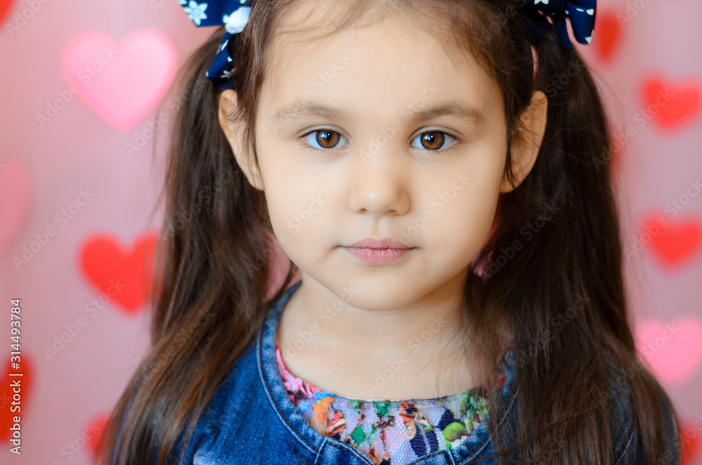 A portrait of little happy girl with long dark hair on the pink background with red hearts. Saint Valentine's day. A portrait of little happy girl with long dark hair on the pink background with red hearts. Saint Valentine's day.