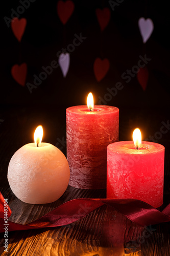 Three wax flame candlelight with ribbon in dark romantic light on hearts background  love dating  Valentine s day  selective focus