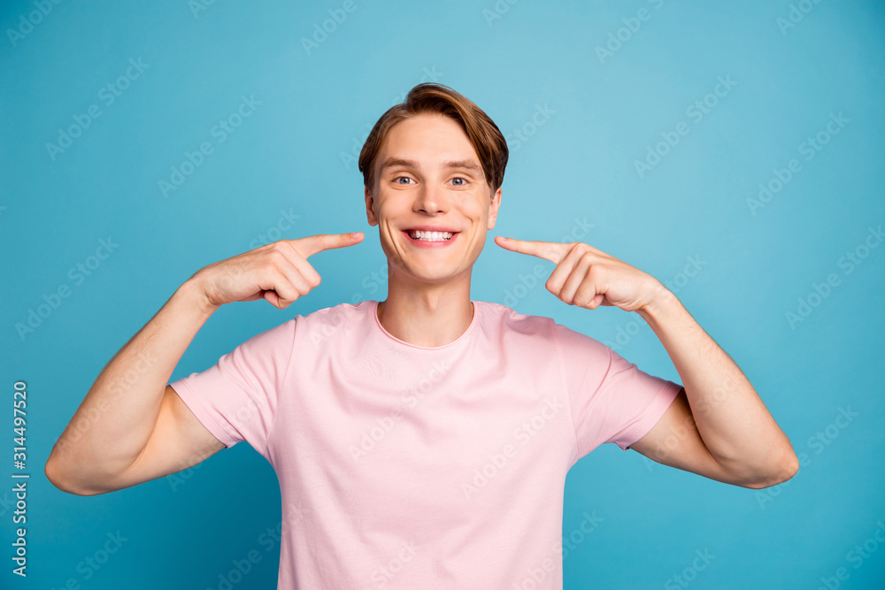 Portrait of positive cheerful guy have orthodontic medical teeth treatment show index finger beaming smile mouth wear stylish clothes isolated over blue color background Portrait of positive cheerful guy have orthodontic medical teeth treatment show index finger beaming smile mouth wear stylish clothes isolated over blue color background