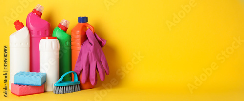 Foto Bottles with detergent and cleaning supplies on yellow background, space for tex