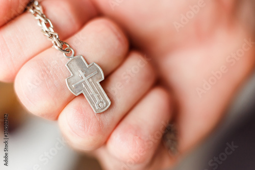 Silver cross in the hand with focus on the cross, shallow DOF