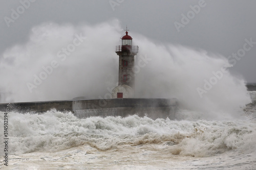 Wind spray after big ocean wave crash. Old Douro river mouth lighthouse and pier, Oporto.
