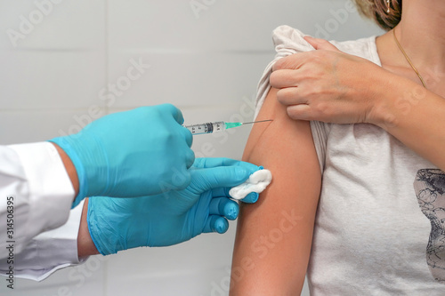 Vaccination healthcare concept. Hands of doctor or nurse in medical gloves injecting a shot of vaccine to a woman patient. Healthcare and medical concept - doctor doing vaccine to patient.