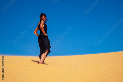 freedom concept, beautiful and happy girl jumping in the sand, in a black dress, joyful emotions