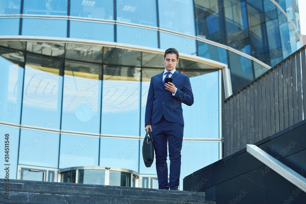 Succesfull young businessman with case tapping message outside business center