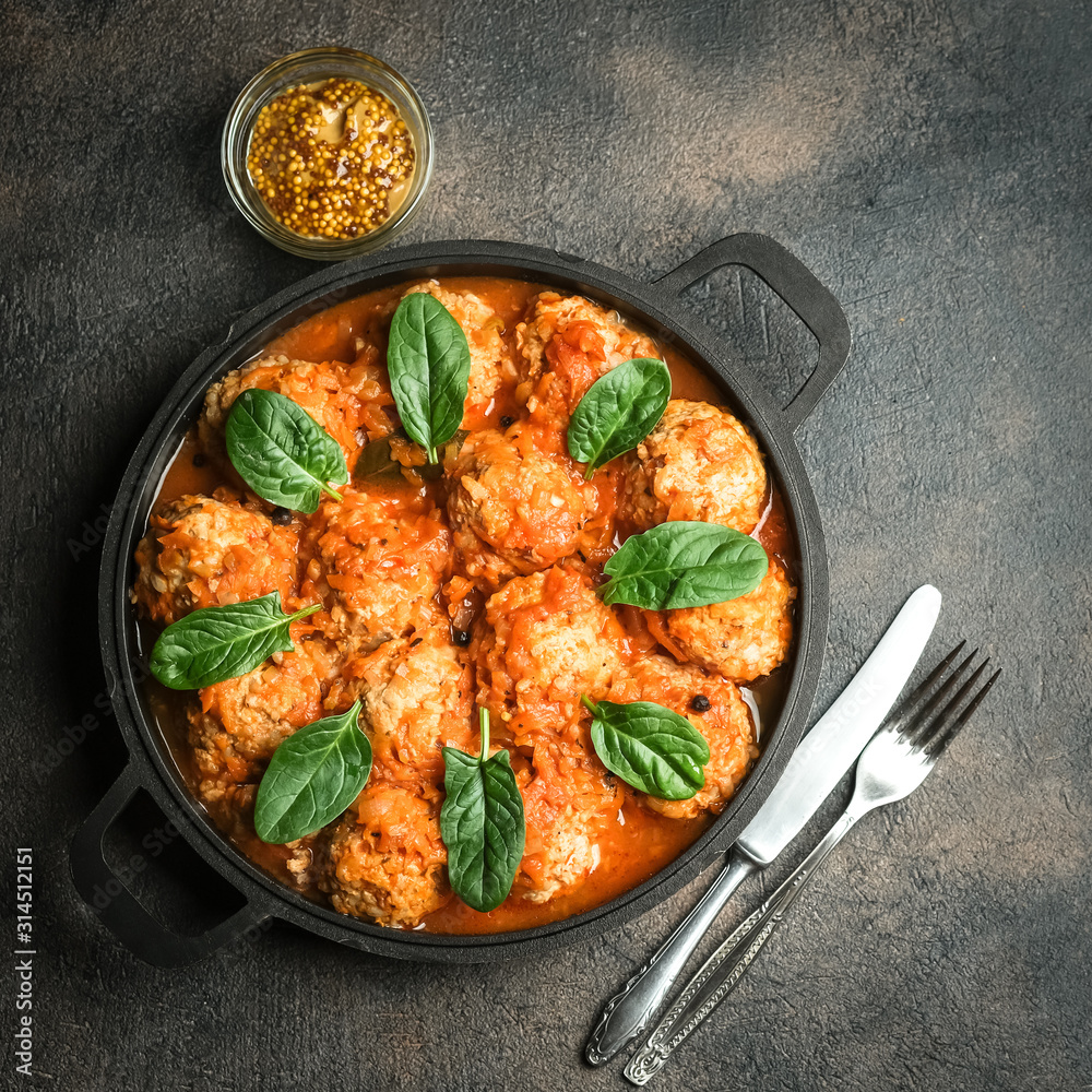 Meatballs in tomato sauce with bazil leaf in a frying pan on dark background. Top view.