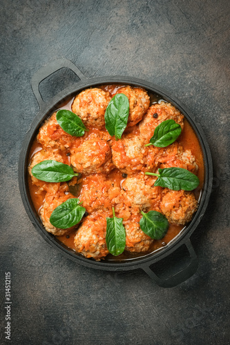 Meatballs in tomato sauce with bazil leaf in a frying pan on dark background. Top view. Copy space.