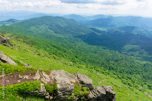 mountain landscape in summer. view from the top of carpathian watershed ridge in to the distance. boulders on the green grassy slopes. sunny weather with clouds on the blue sky