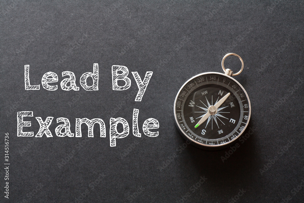 Written Lead By Example words on black background with compass