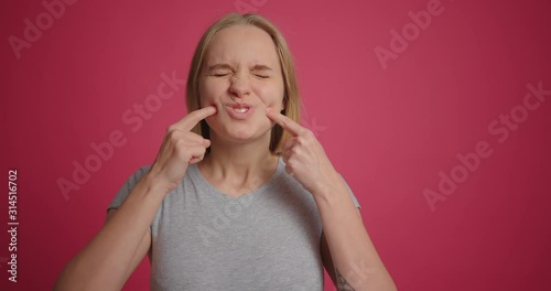Blonde girl being funny and puffing out her cheeks at pink wall background