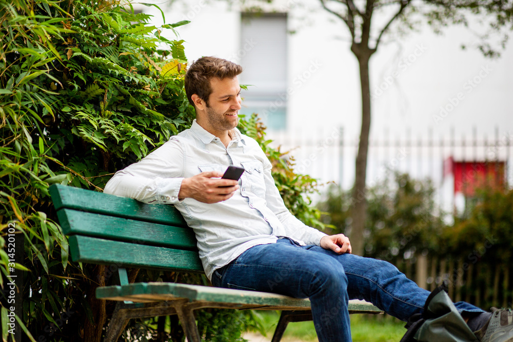 happy man sitting on park bench with cellphone