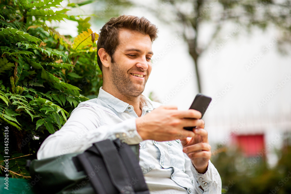 Close up handsome man sitting looking at mobile phone while sitting on park bench Close up handsome man sitting looking at mobile phone while sitting on park bench